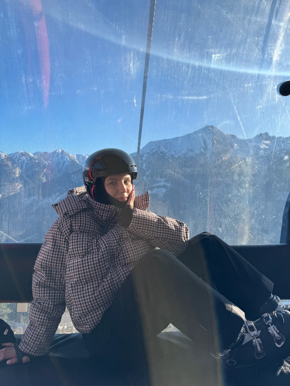 Me wearing a ski helmet and ski boots inside a gondola, with mountain ridges visible through the window.