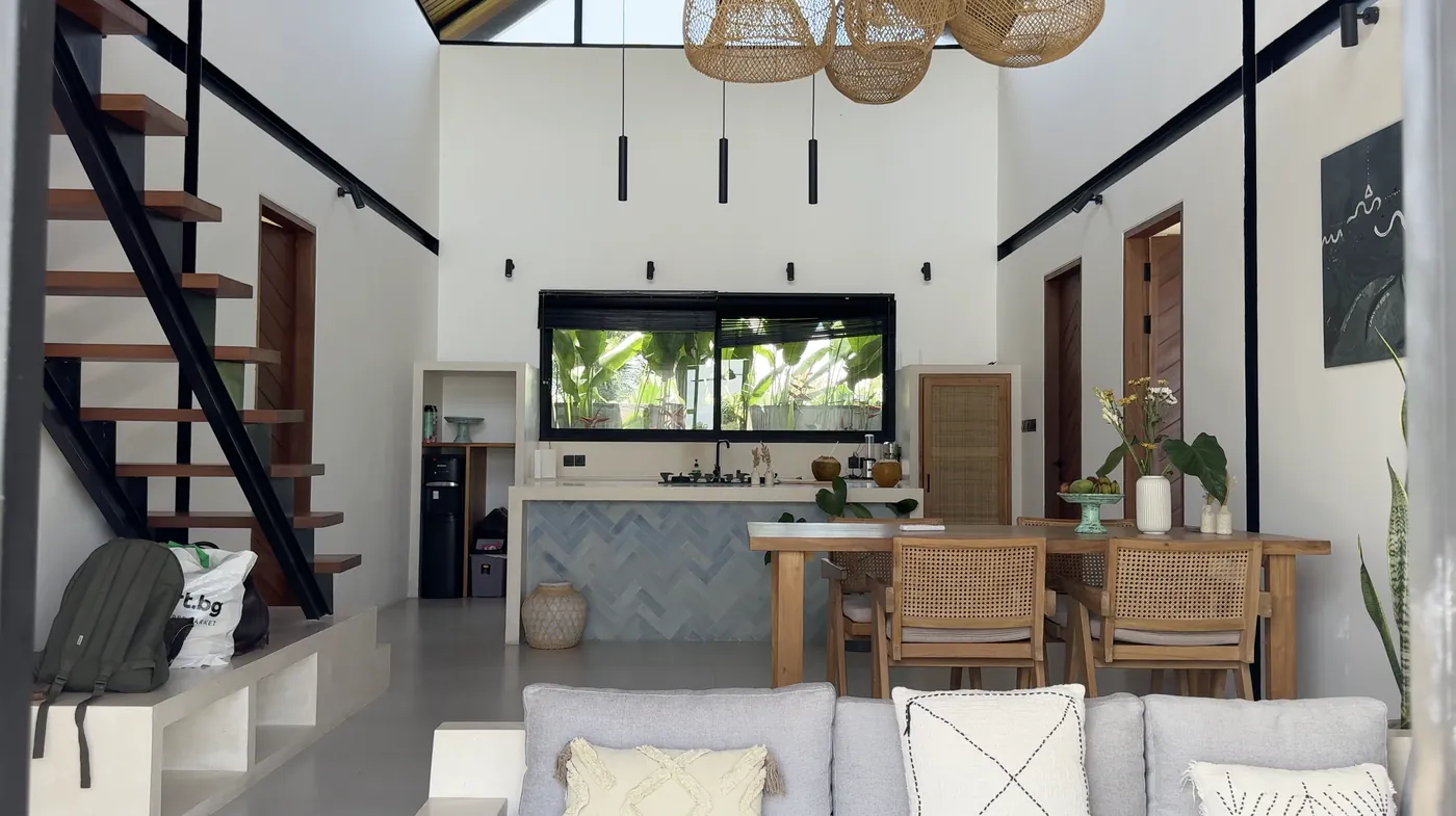 A bright living room with a wooden table, a staircase and rattan lamps