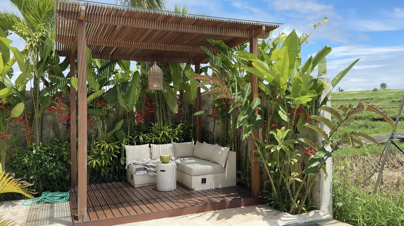 A wooden pergola with a white sofa surrounded by tropical plants