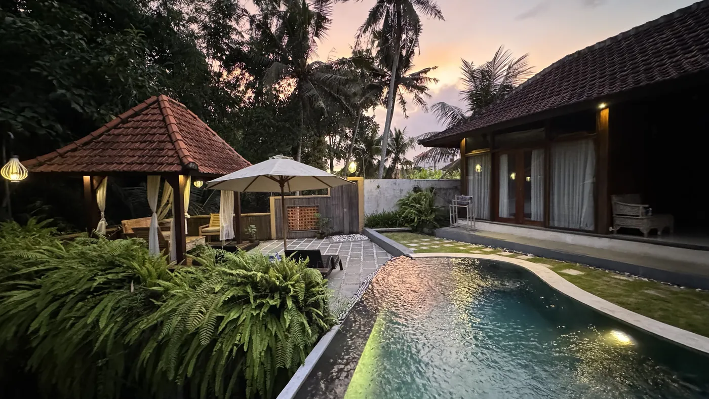 A villa with warm lights and a pool at dusk among palm trees