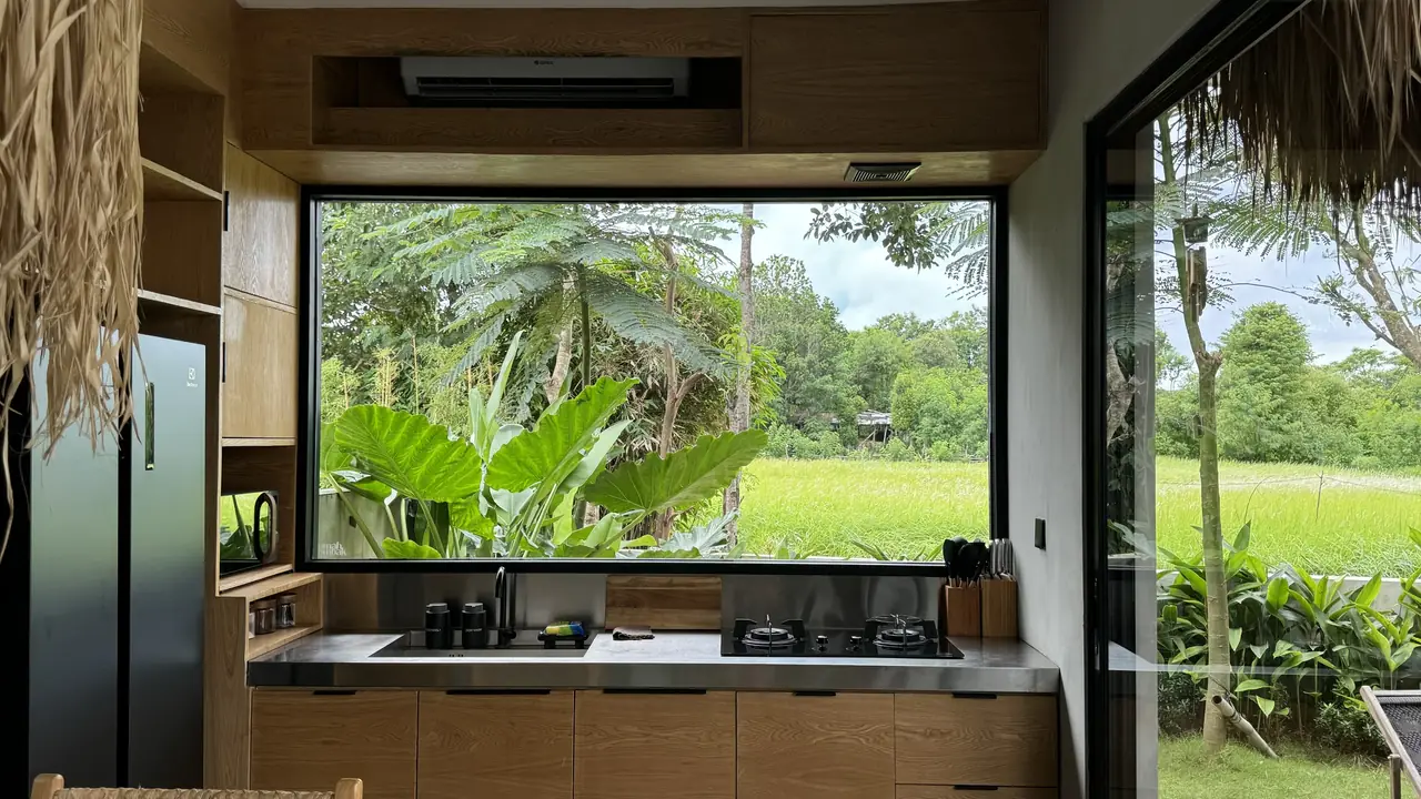 A kitchen with a large window over a green rice field and palm trees