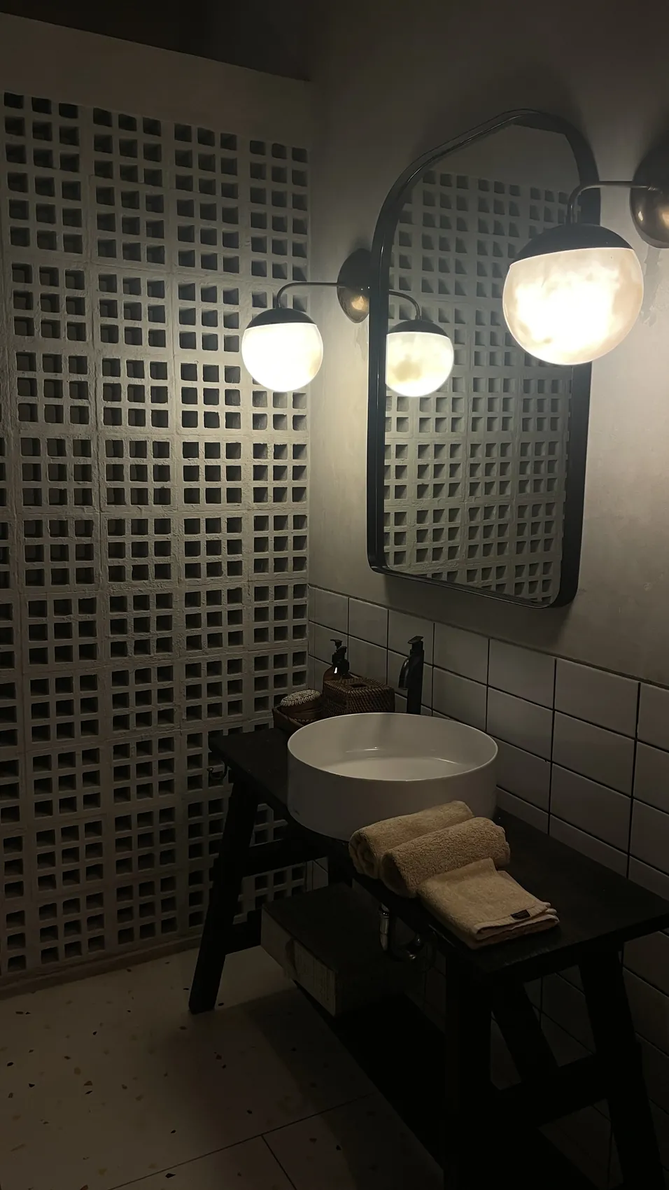A bathroom with a round white basin, a mirror and two wall lamps