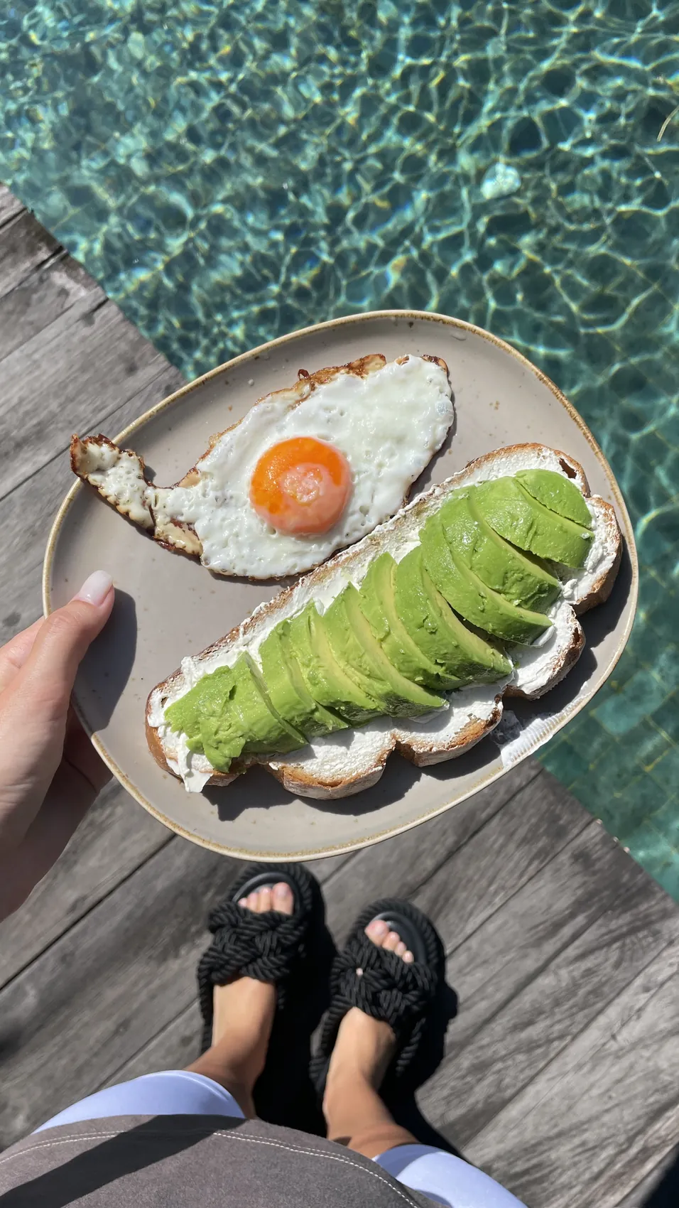 Avocado toast and a fried egg on a plate on the edge of the pool