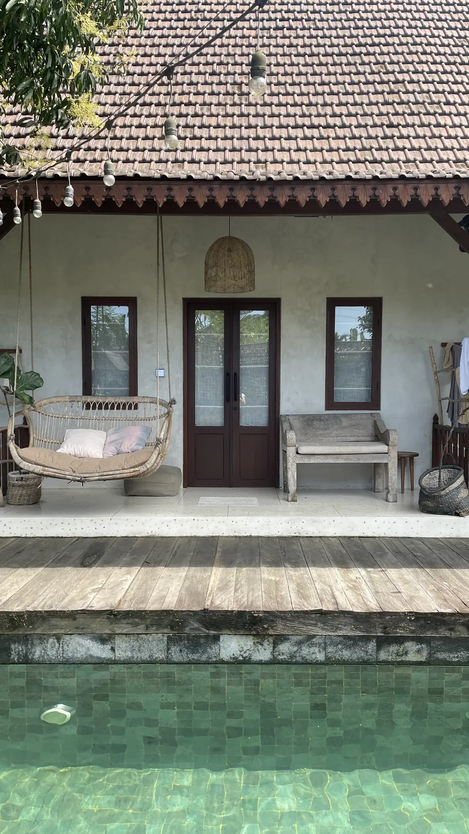 The front of a villa with a tiled roof, a hanging chair and a wooden bench on the terrace