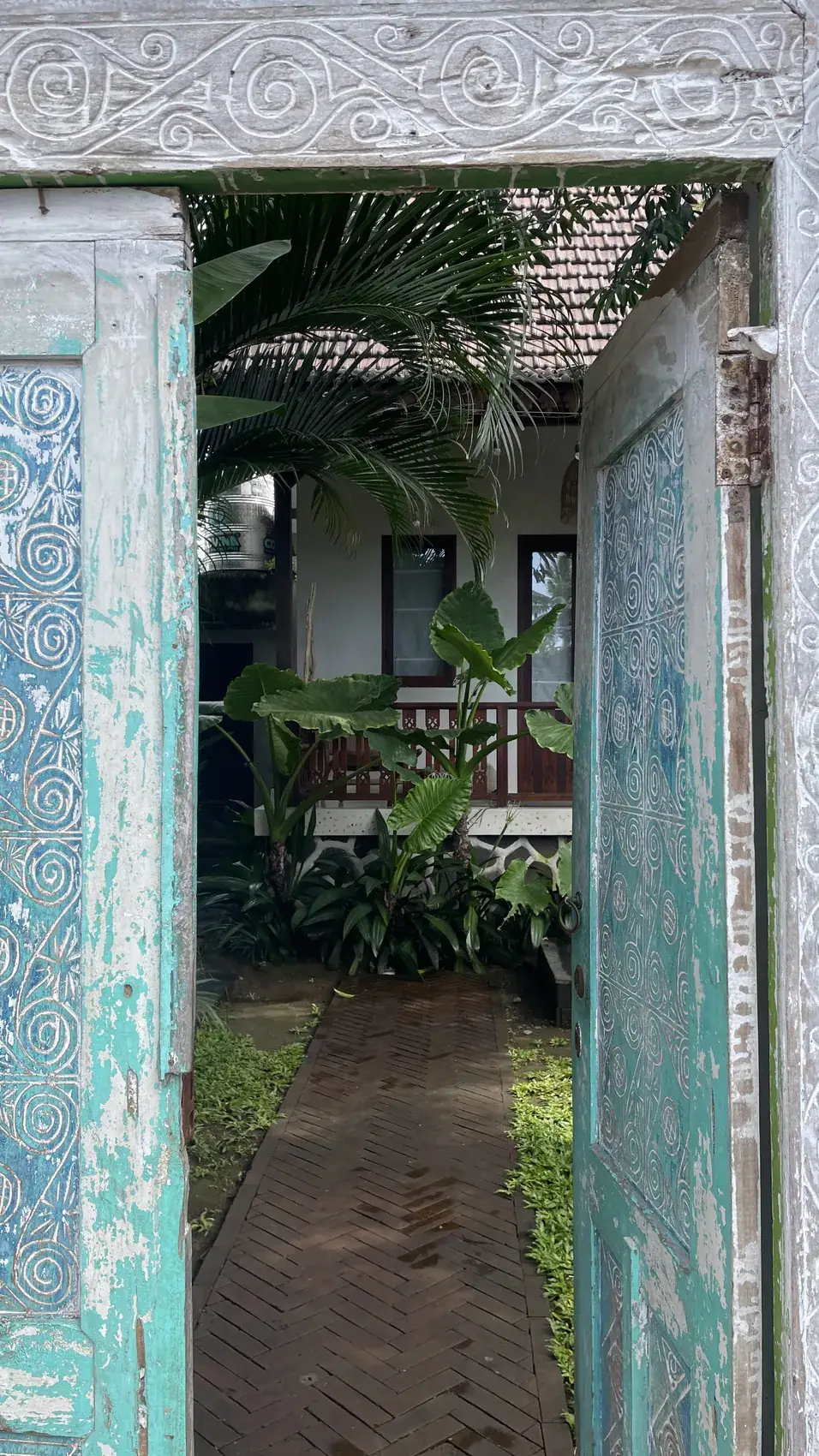 A carved wooden gate door opening onto a garden path to a villa