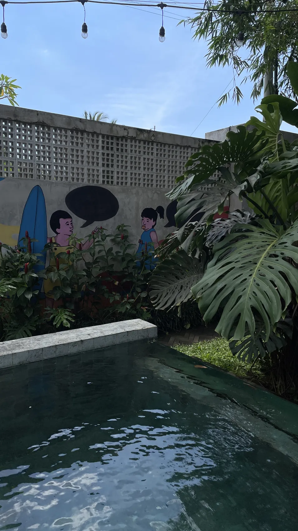 A small pool with a wall painted with surfing characters and tropical plants