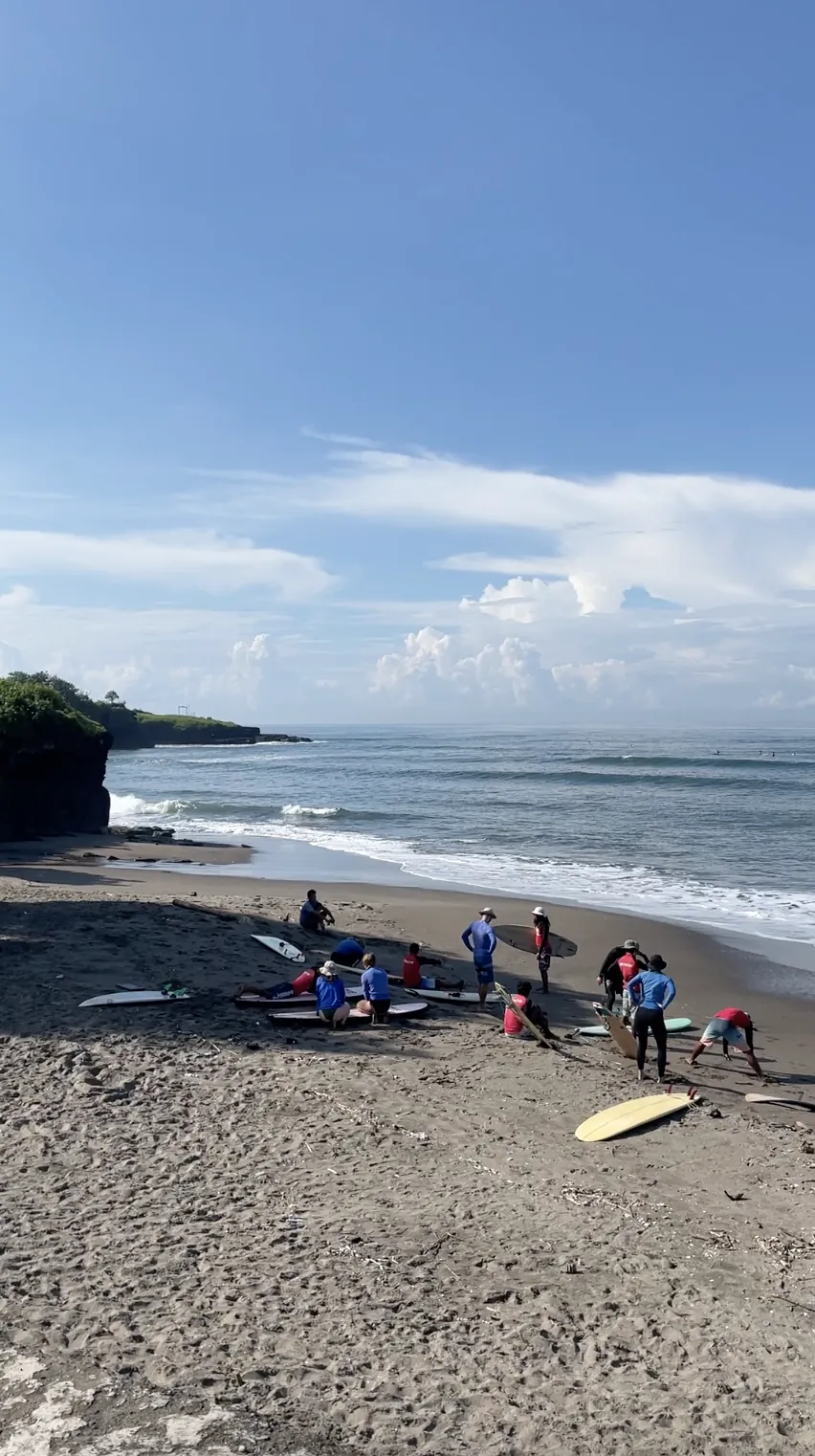 Surfers practising on dark sand with the ocean behind