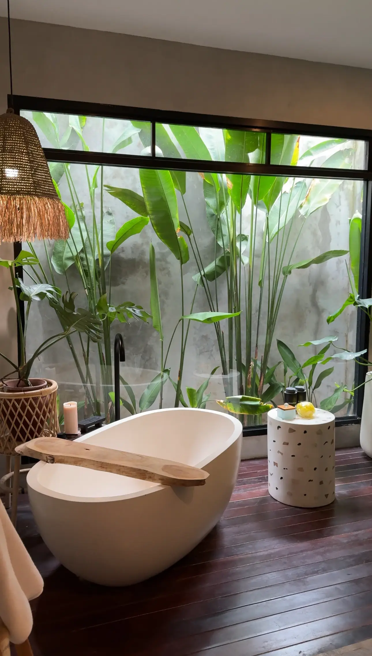 A white freestanding tub in front of a window with green banana plants