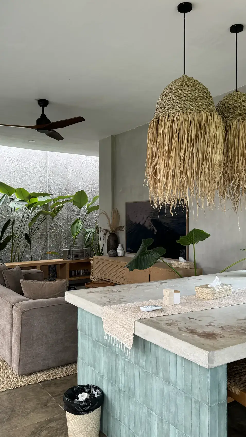 A living area with straw pendant lamps, a ceiling fan and a sofa next to a kitchen island