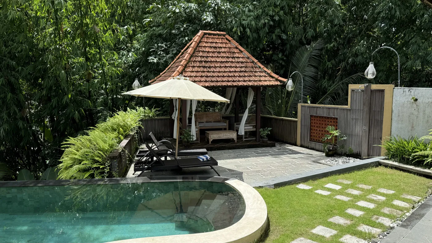 A red-tiled pavilion with an umbrella and sun loungers next to a pool