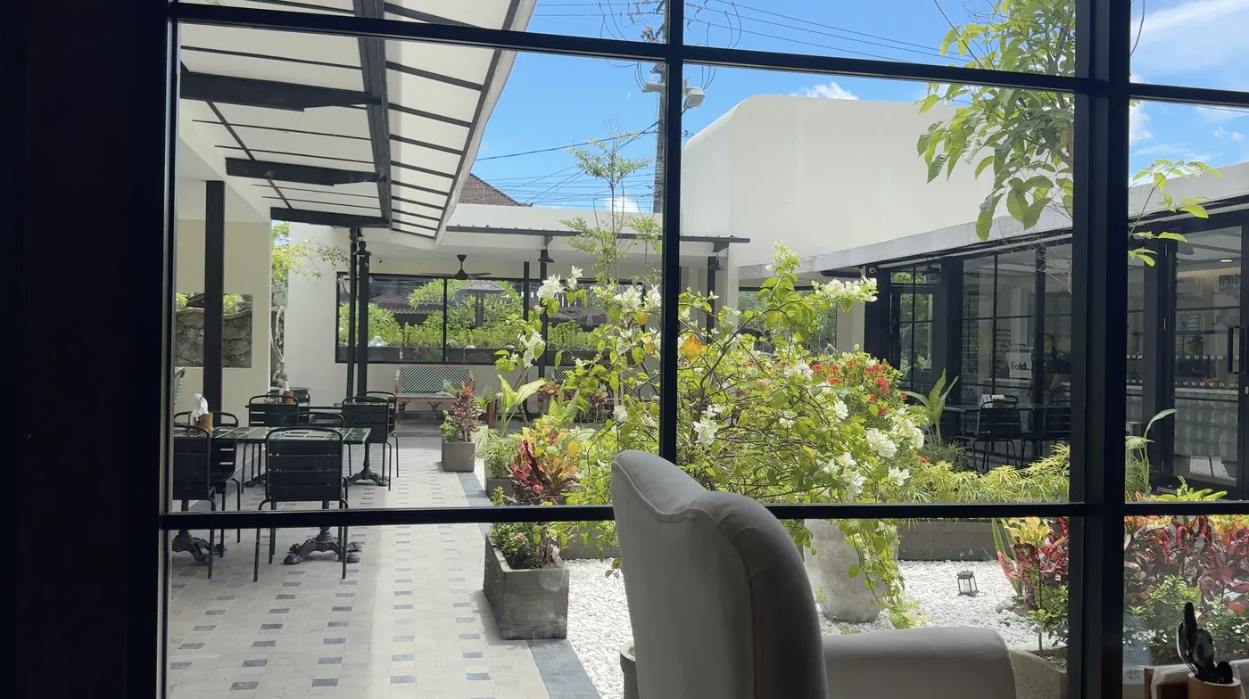 A bright courtyard with flowering plants seen through a large black-framed window