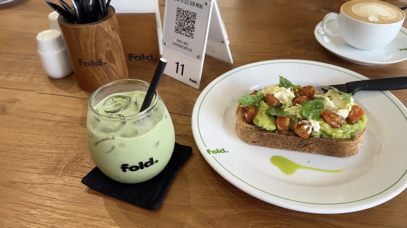 Avocado toast with tomatoes next to an iced matcha drink and a cappuccino