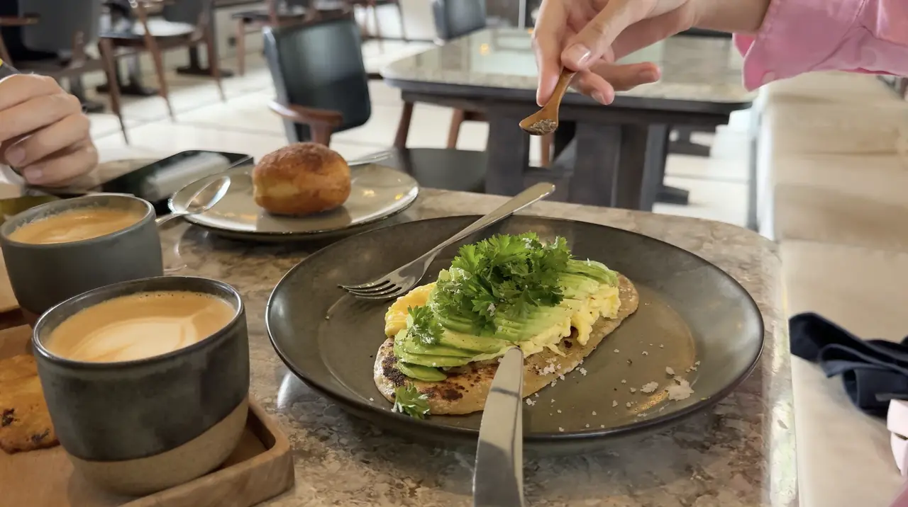 Avocado and scrambled eggs on toast next to two cups of coffee on a marble table