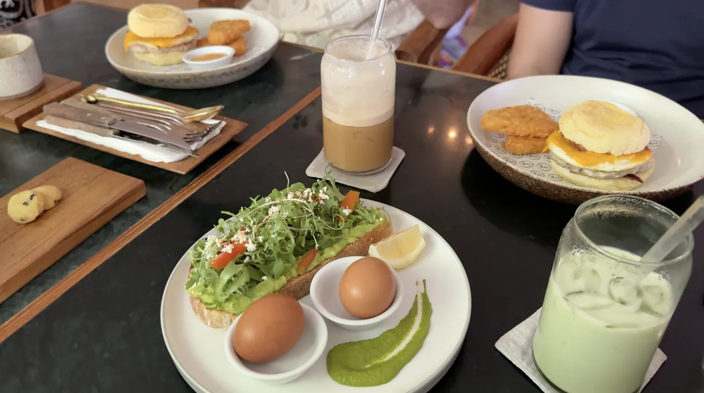 Avocado toast with two eggs, an iced coffee and an iced matcha on a dark table