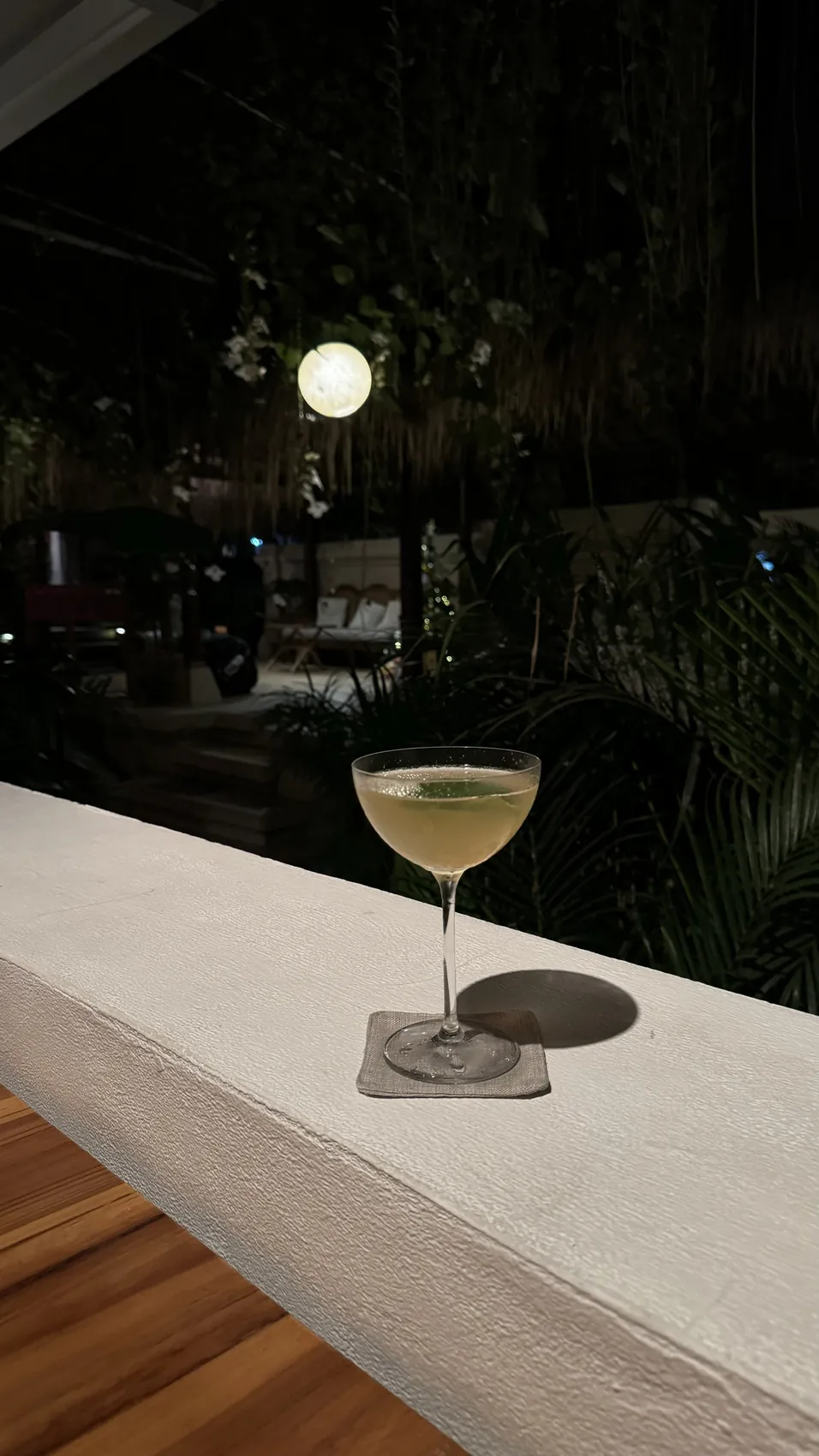 A cocktail on a white ledge at night with palms behind