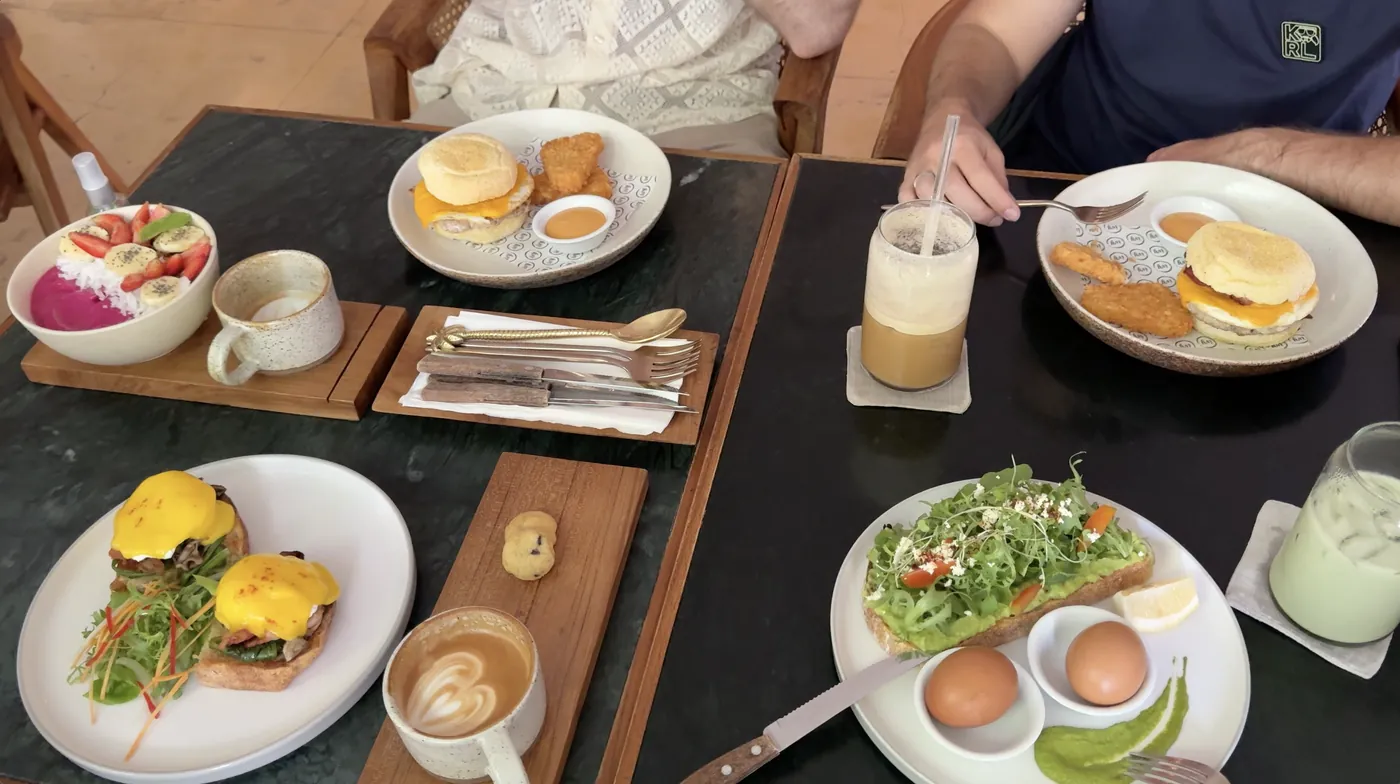 A dark table with avocado toast, an egg muffin, a smoothie bowl and benedict eggs