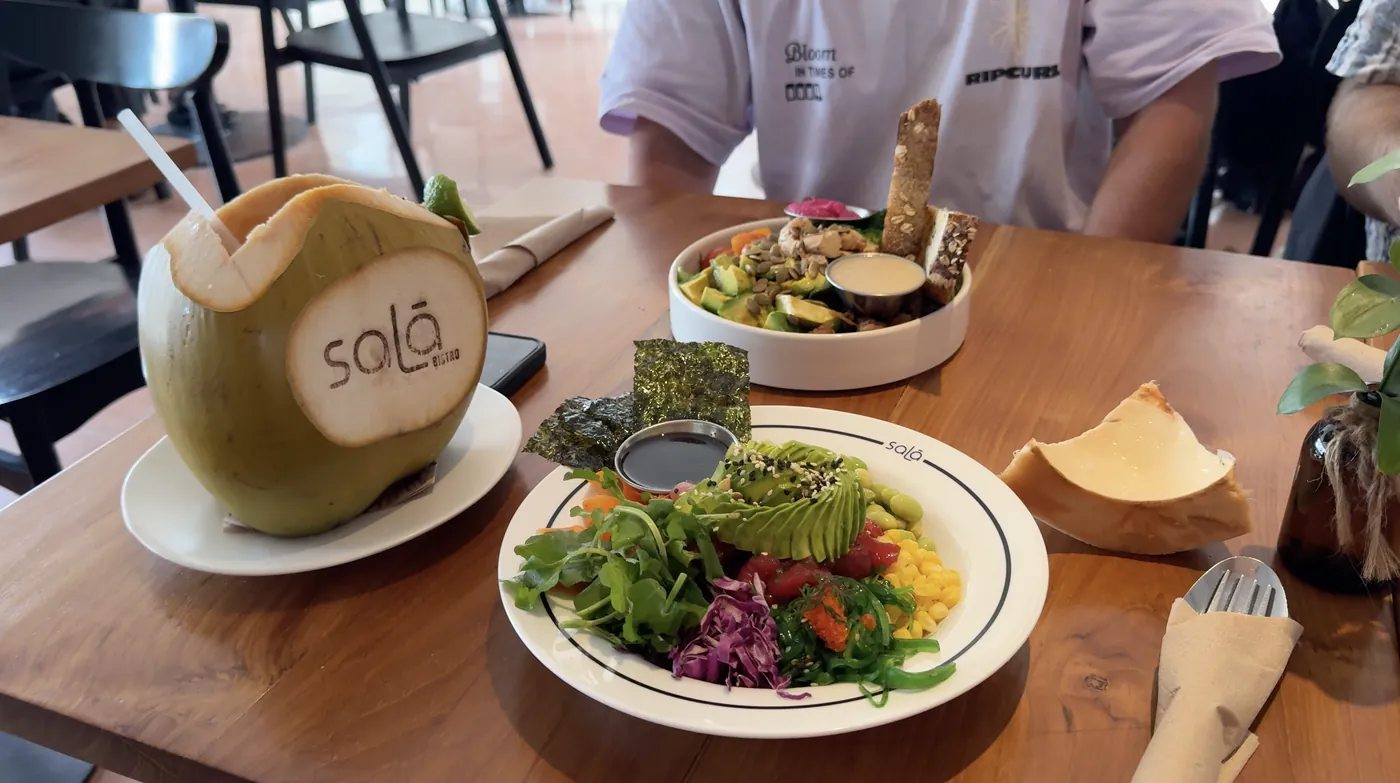 A fresh coconut with the Sala logo next to two lunch bowls