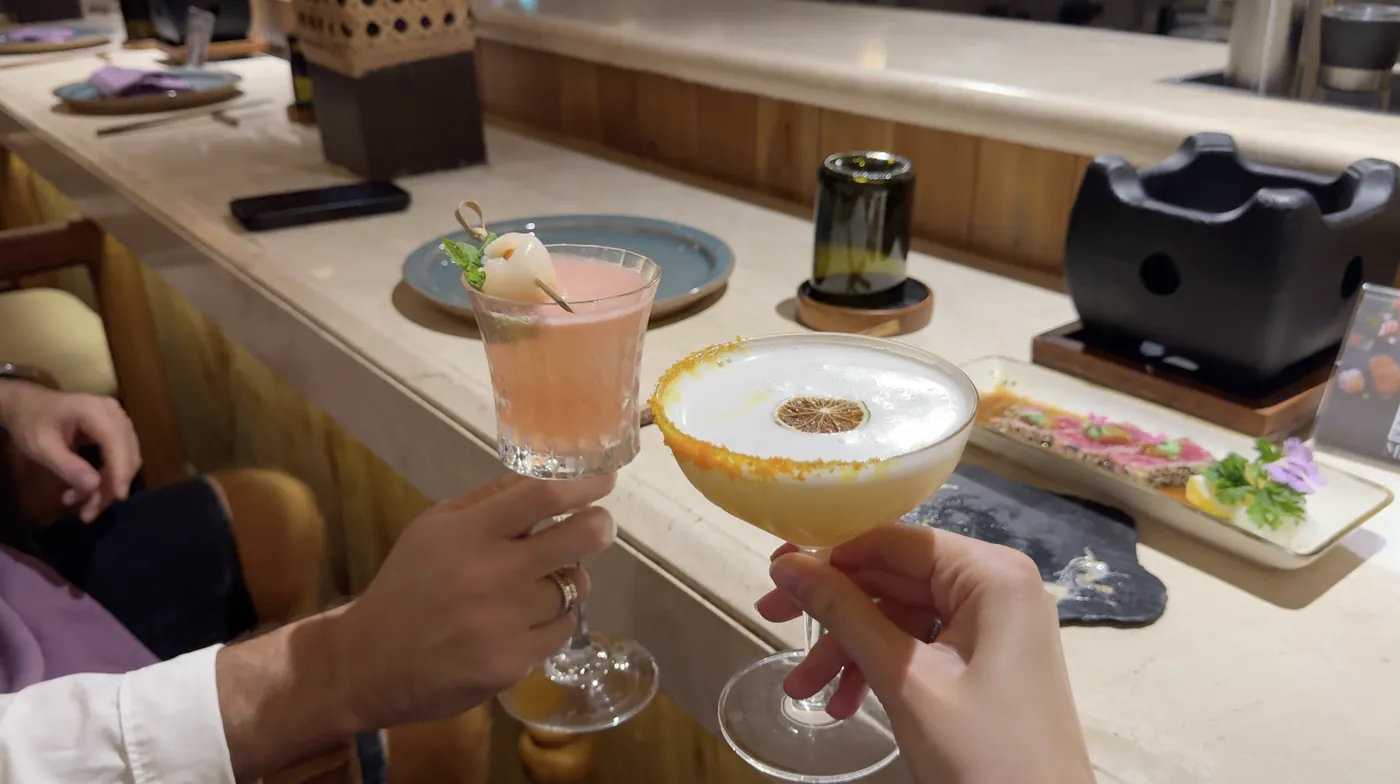 Two cocktails held up in front of plates of sushi