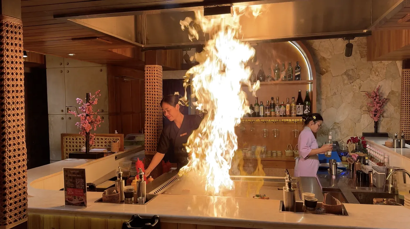 A chef cooking on a grill with a tall flame in an open kitchen
