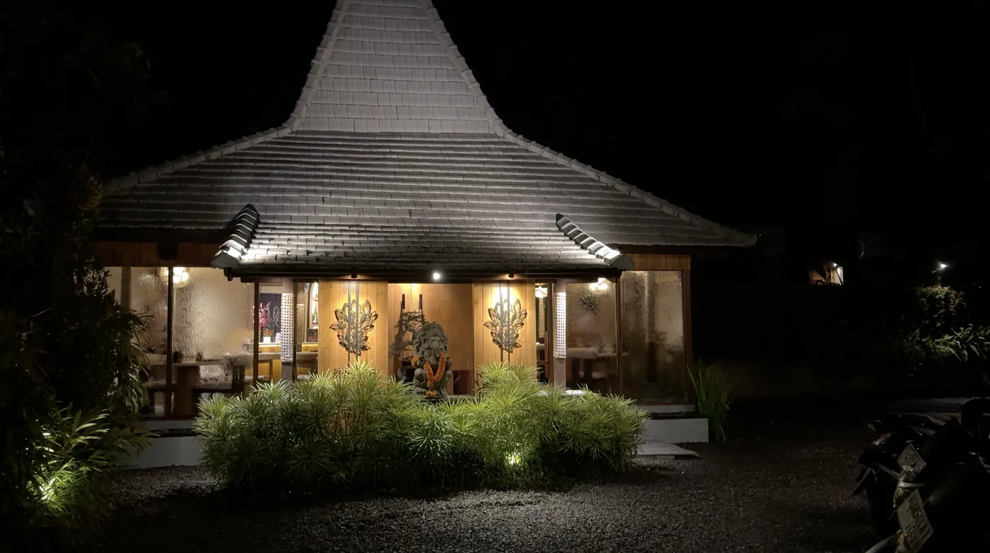 A Japanese restaurant with a pointed roof lit up at night among plants