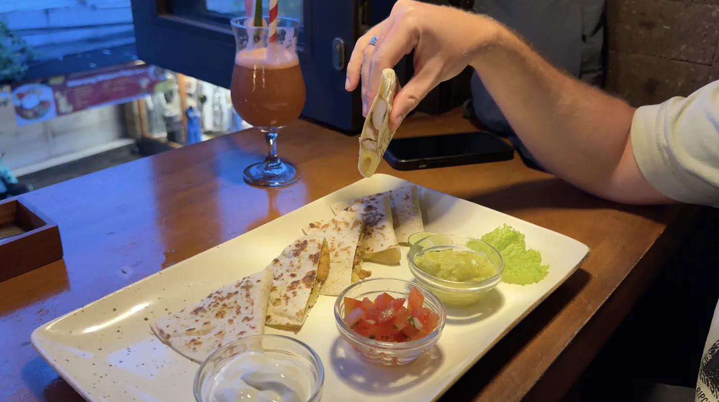 A plate of quesadilla slices with salsa and guacamole next to a drink