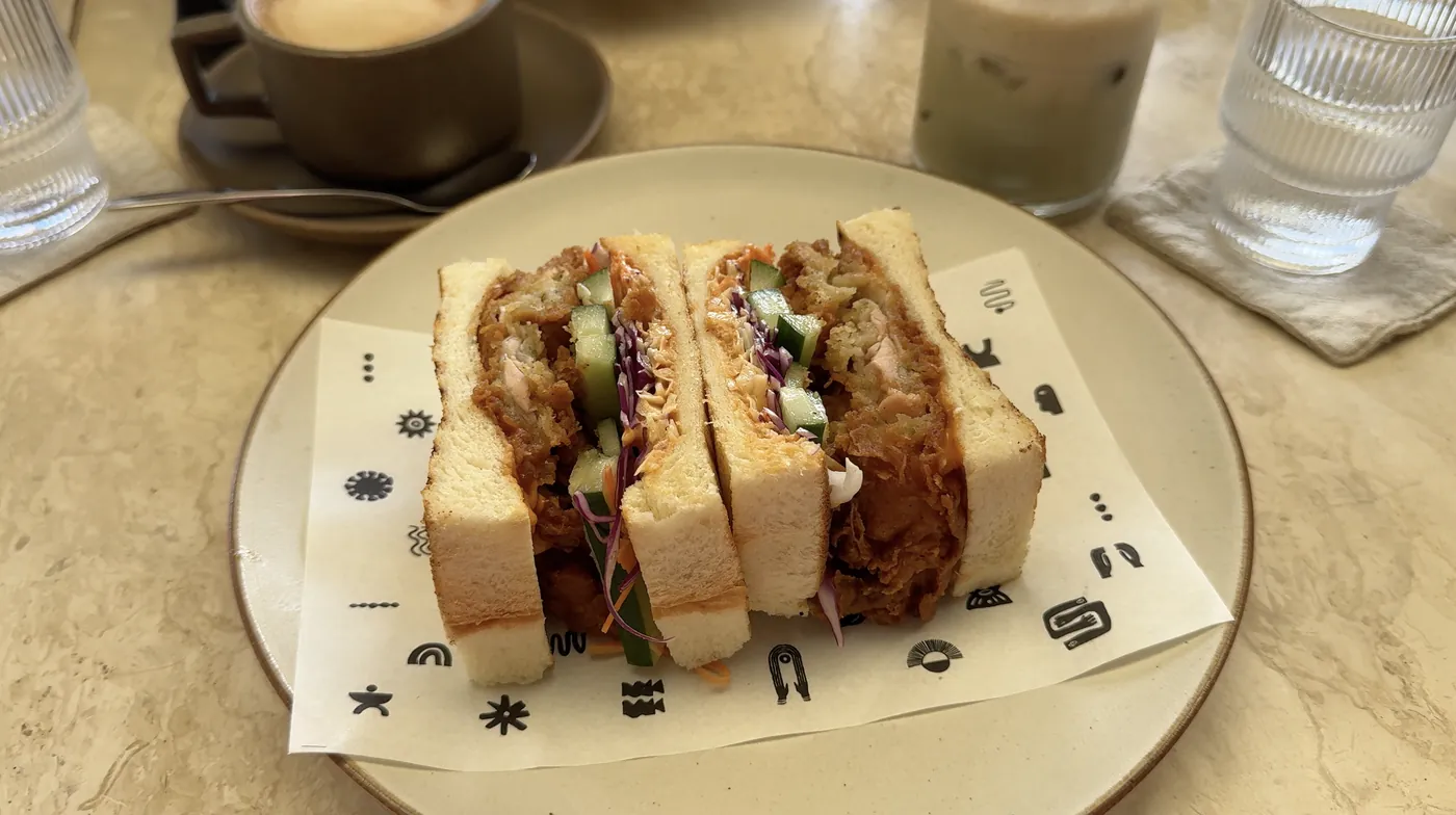A sandwich with crispy chicken and red cabbage on a plate with a coffee