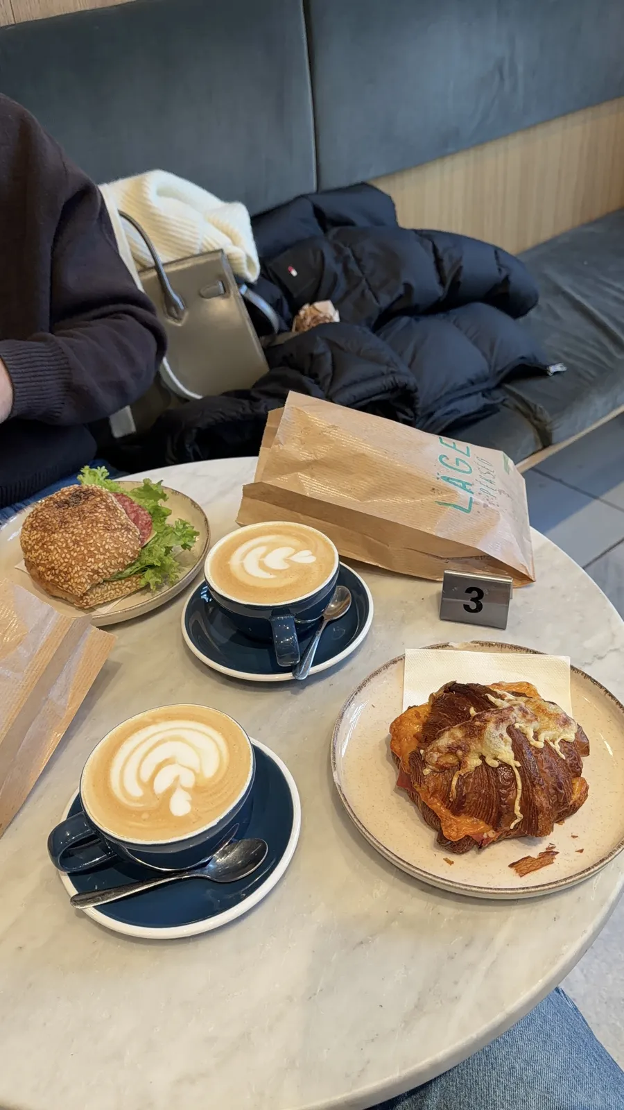 A marble table with two cappuccinos and pastries on plates.