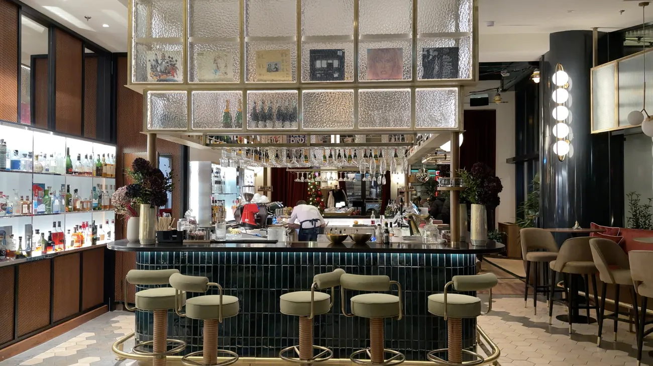 A bar with a green counter, high stools and shelves of bottles.
