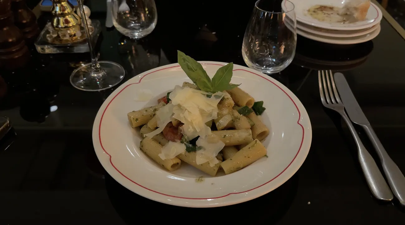 A plate of rigatoni with cheese and a basil leaf beside cutlery.