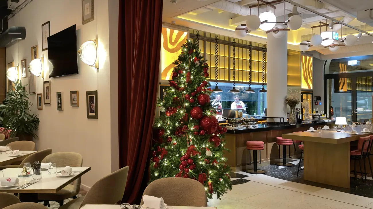 A dining room with a decorated Christmas tree, tables and a bar in the background.