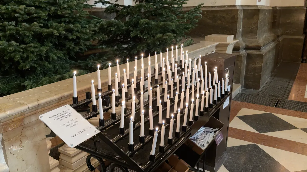 Rows of lit candles on a stand with a small notice beside them.