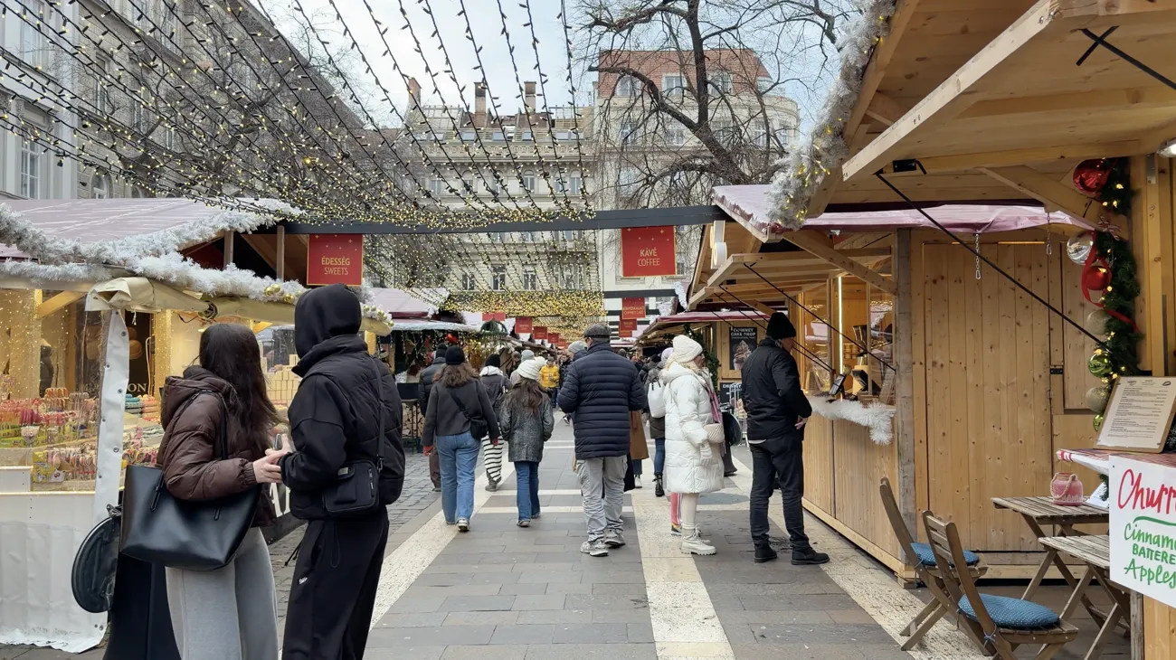 Visitors walking along a lane of wooden market stalls under strings of lights.