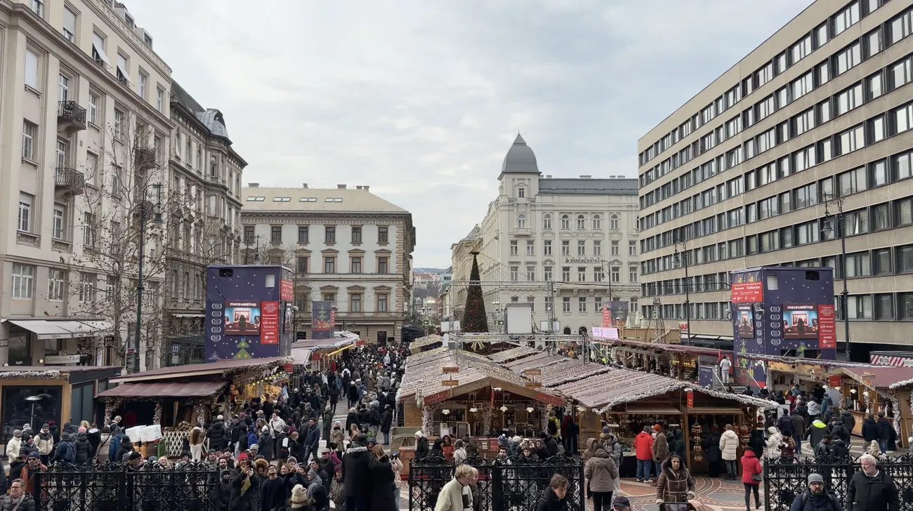 A busy Christmas market with wooden stalls in a city square lined with historic buildings.