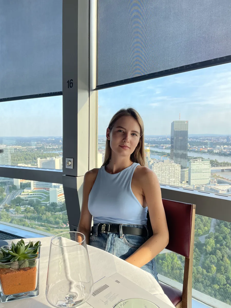 A woman seated beside the restaurant window with Vienna and the river behind her.