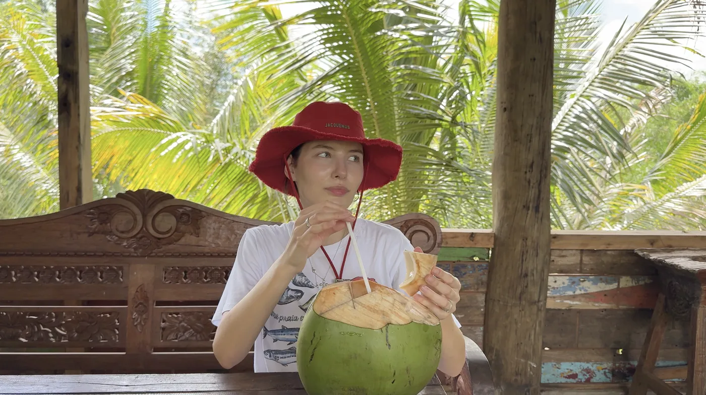 Me in a red hat drinking from a fresh coconut at a wooden table