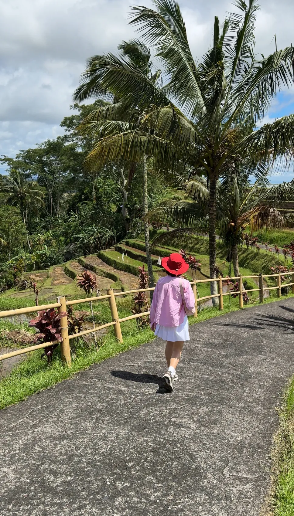 Me in a red hat walking along a paved path above the rice terraces