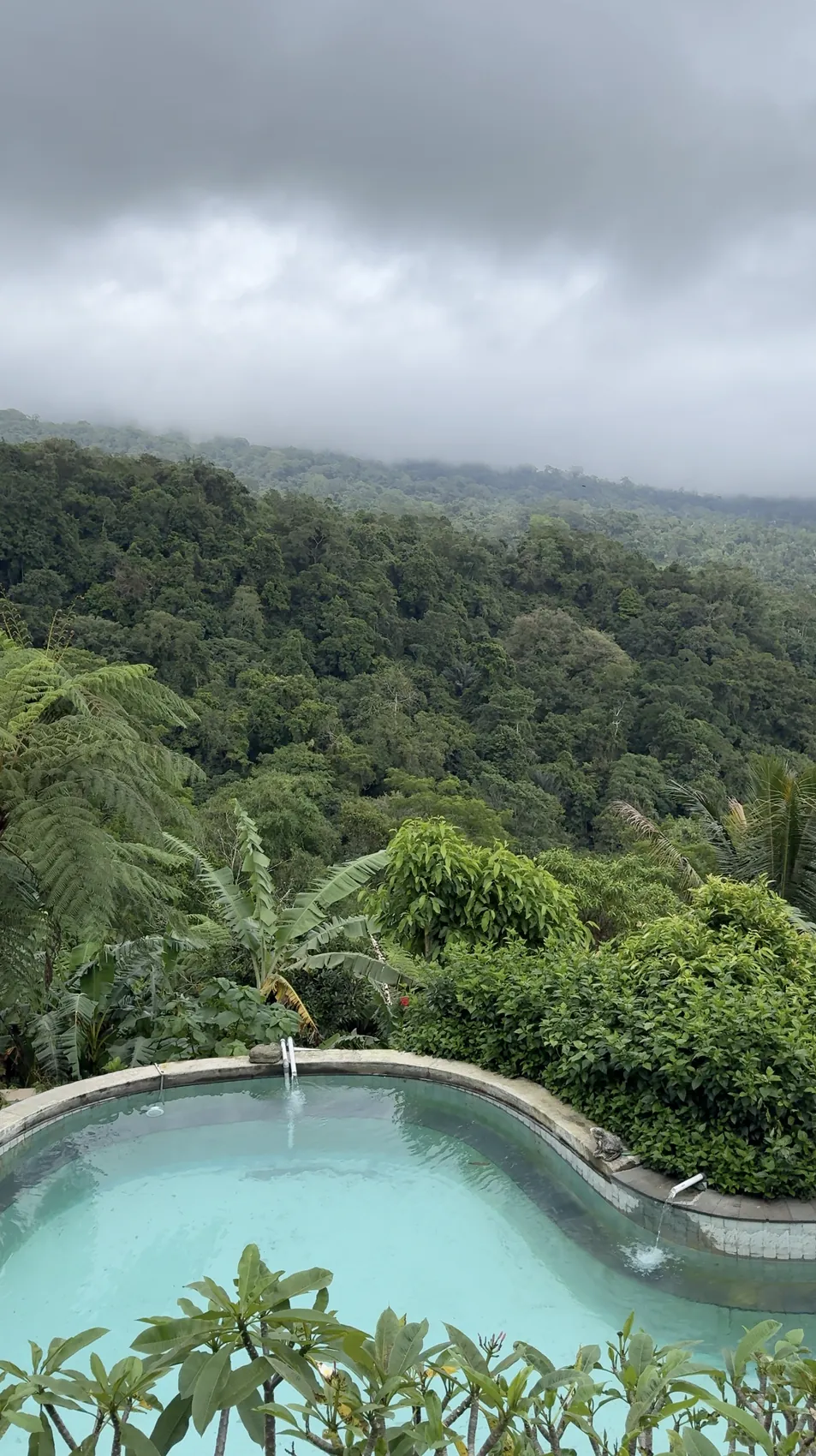 A turquoise pool above a jungle valley under grey clouds