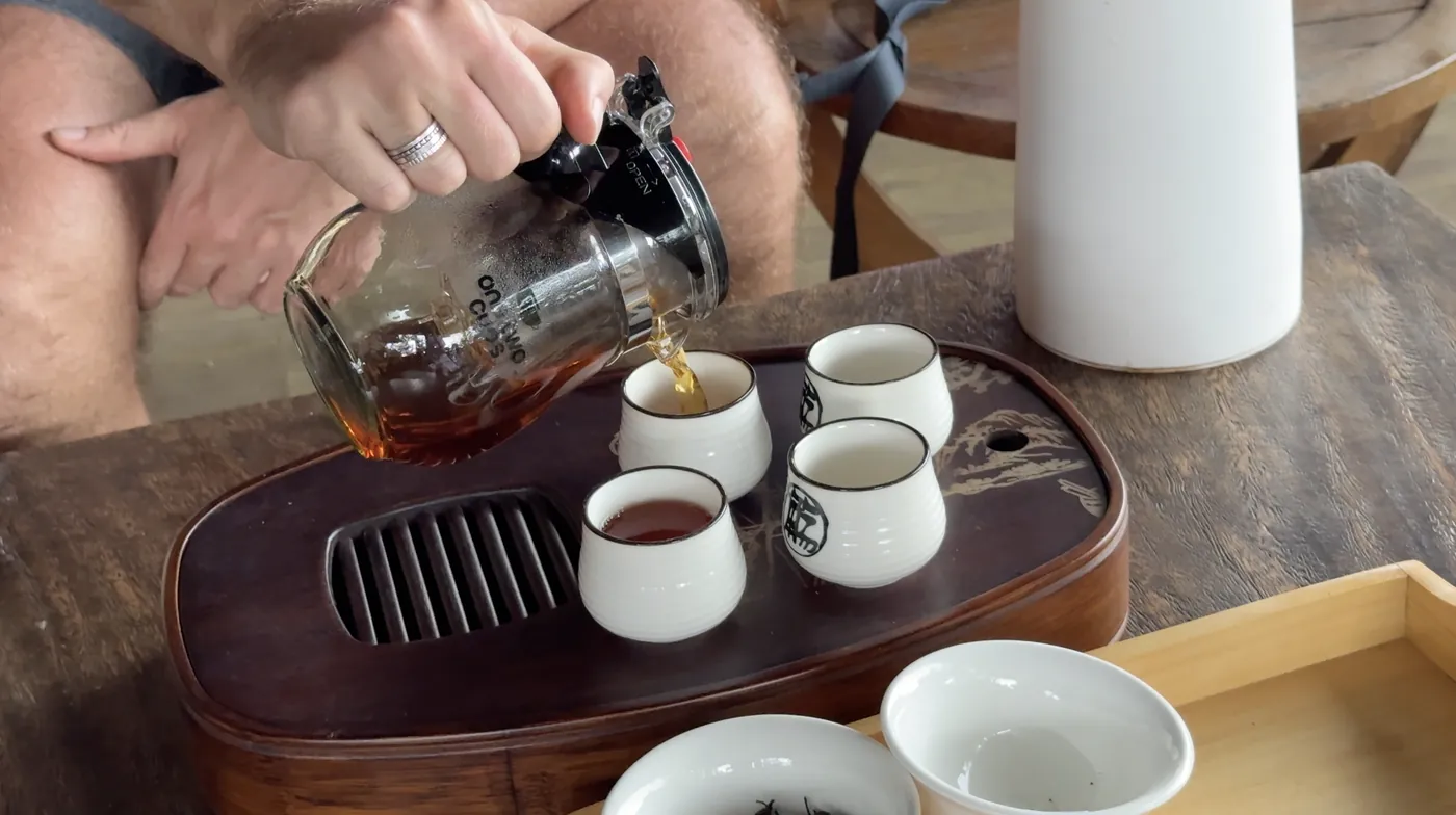 Hands pouring tea into small white cups on a wooden tray