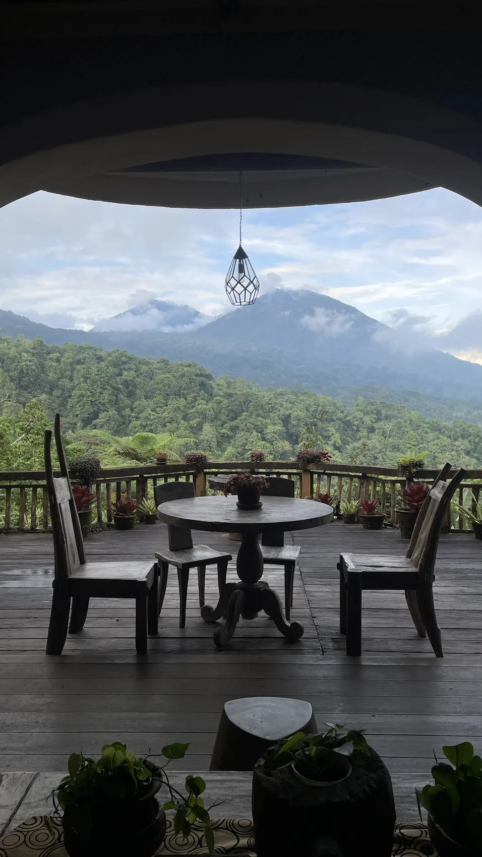 A wooden table and chairs on a terrace looking at a volcano and forest