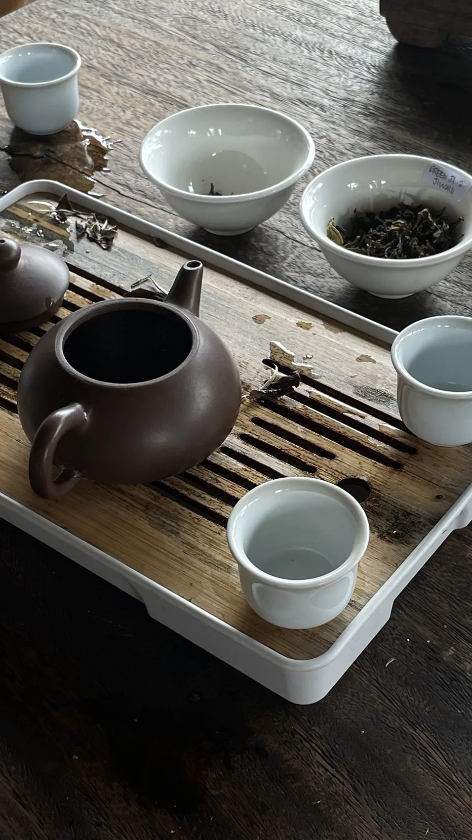 A dark teapot, small white cups and loose tea leaves on a wooden tray