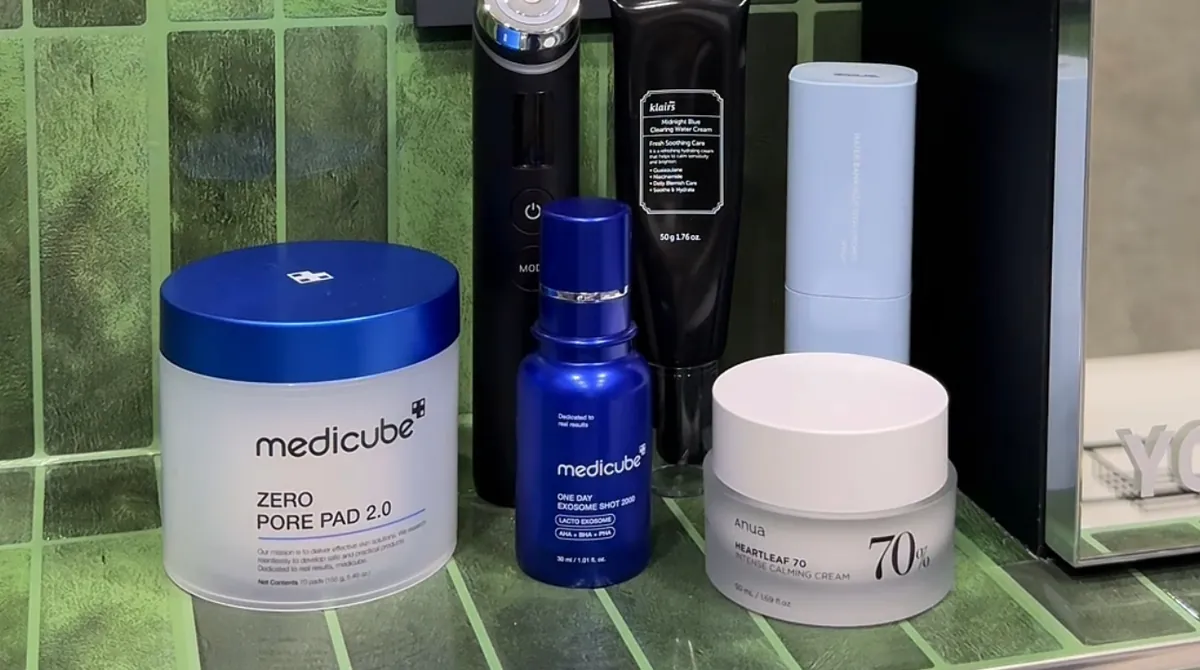 A Medicube Zero Pore Pad 2.0 jar, a blue Medicube bottle, an Anua Heartleaf cream and other skincare on a green-tiled bathroom shelf.