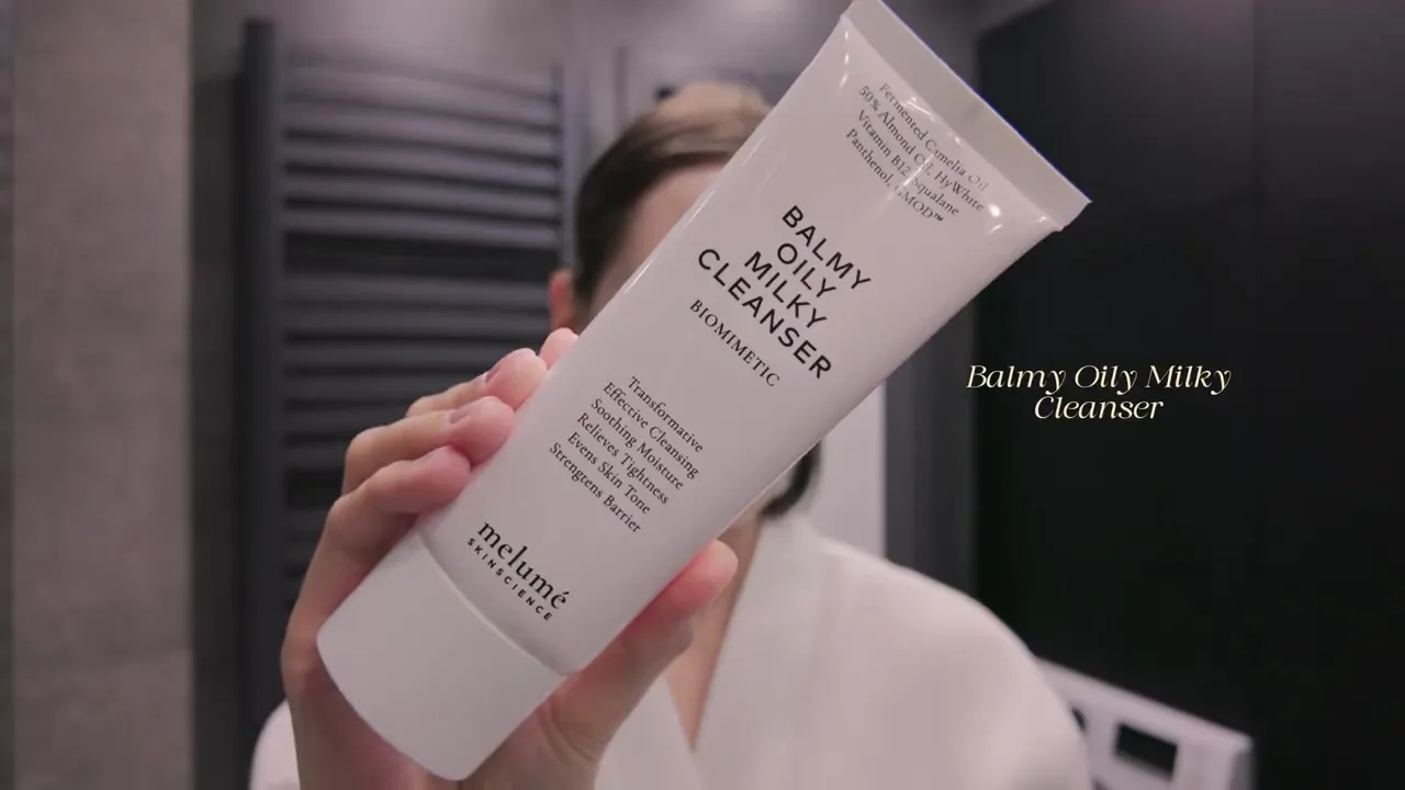 A hand holding a white tube of Melumé Balmy Oily Milky Cleanser.