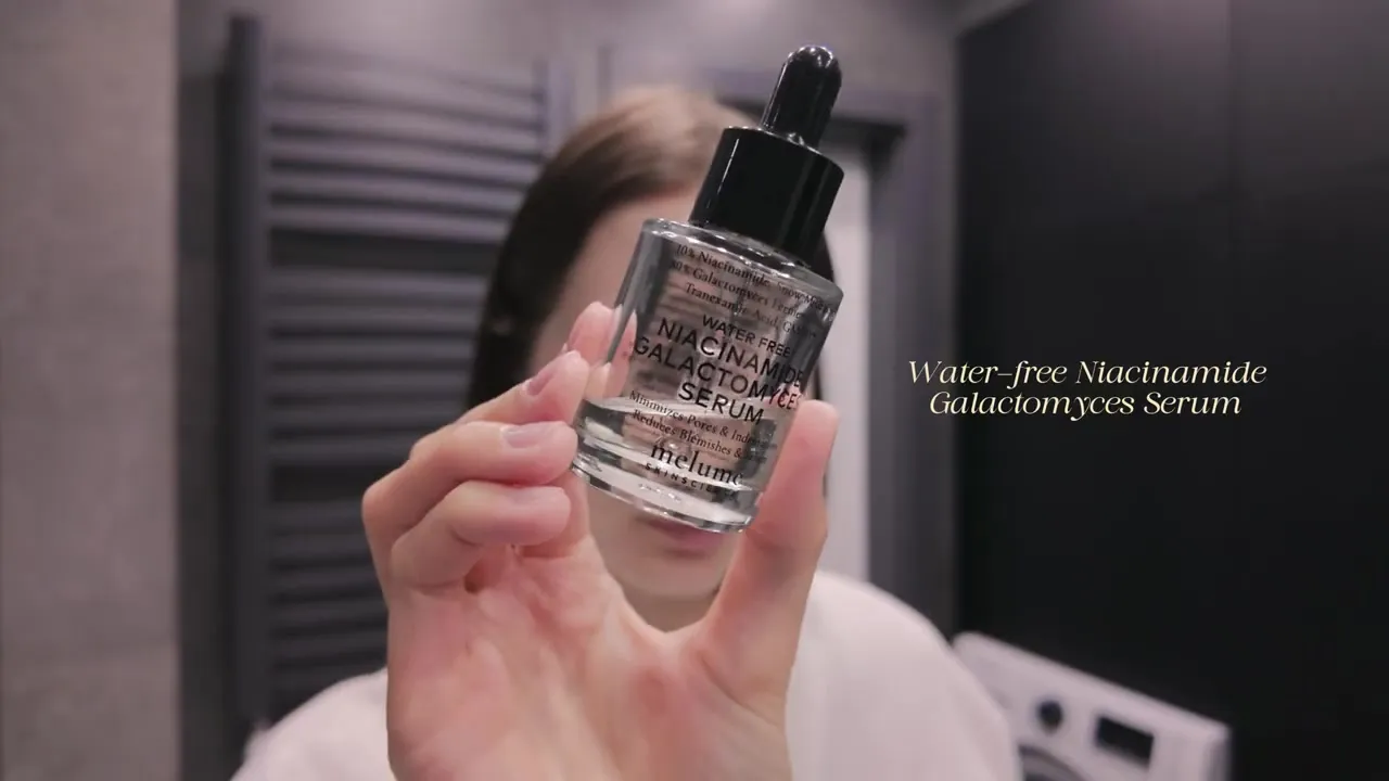 A hand holding a bottle of Melumé Water-free Niacinamide Galactomyces Serum with a black dropper.