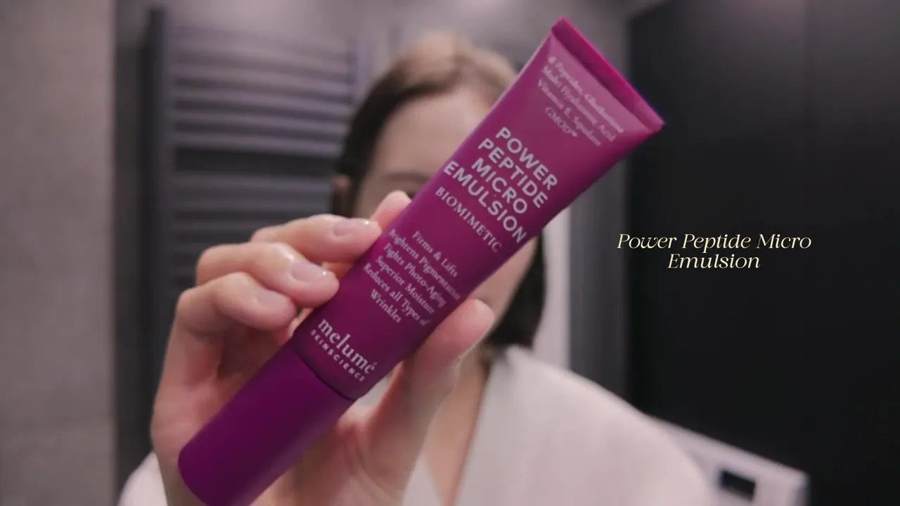 A hand holding a pink tube of Melumé Power Peptide Micro Emulsion.