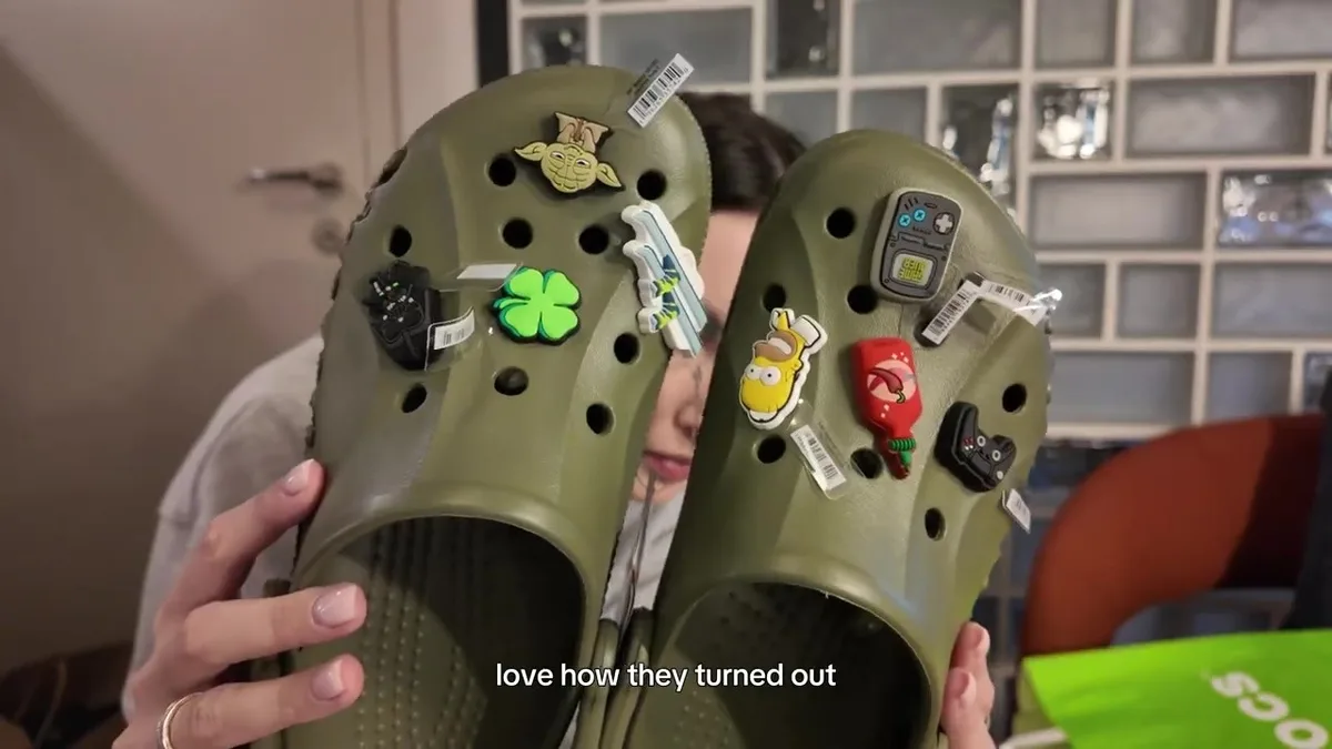 Olive Crocs clogs with eight colourful decorations, including skis, a clover and gaming-themed shapes.