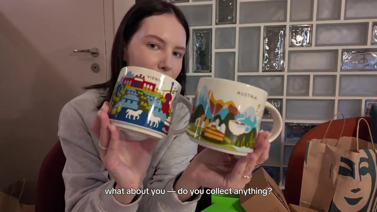 Me holding two Starbucks souvenir mugs labelled Vienna and Austria, with city and mountain illustrations.