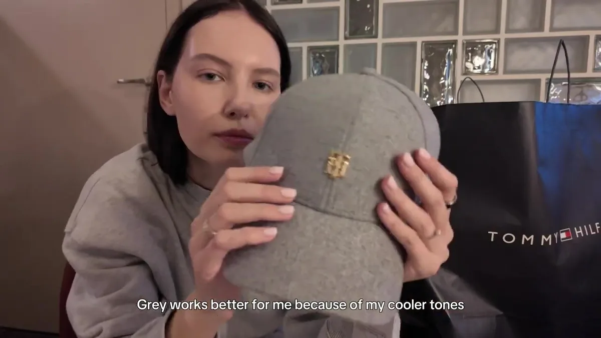 Grey Tommy Hilfiger cap with a small gold-coloured monogram, held by me.