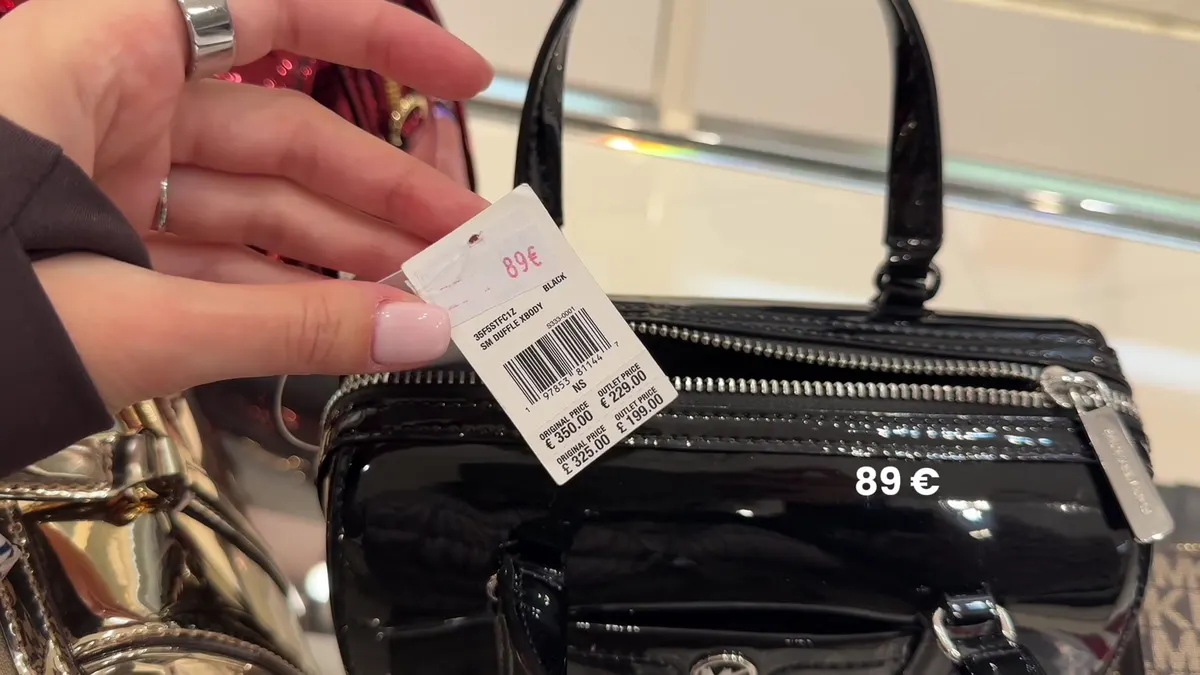 Black Michael Kors Duffle with an €89 marked price and a tag listing original €350 and outlet €229.