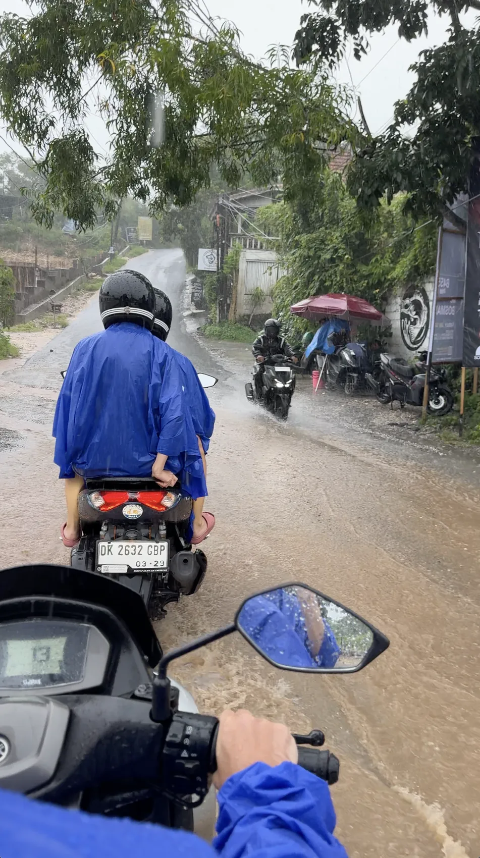 A person in a blue raincoat riding through water on a road