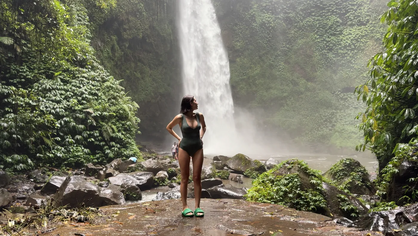 Me in a swimsuit standing on rocks in front of Nungnung Waterfall